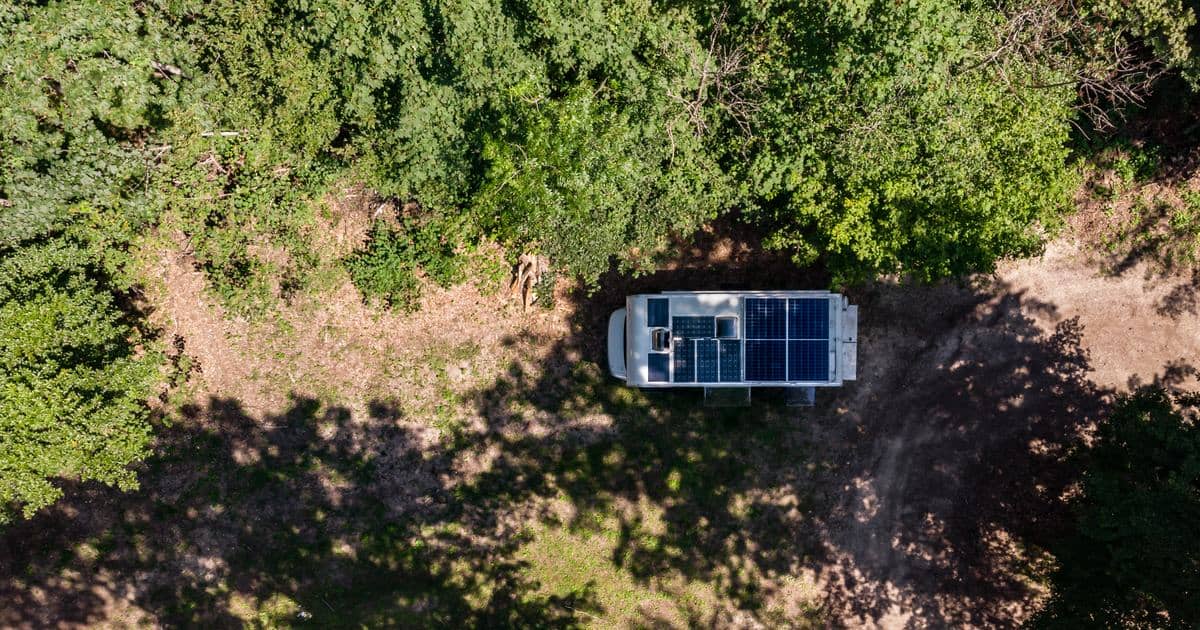 Légifelvétel egy tetőre szerelt napelemekkel felszerelt lakóautóról egy erdei tisztáson