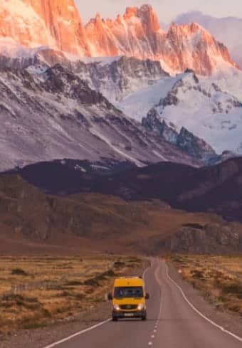 Sárga kempingbusz egy nyílt úton a havas Fitz Roy-masszívum alatt Patagóniában